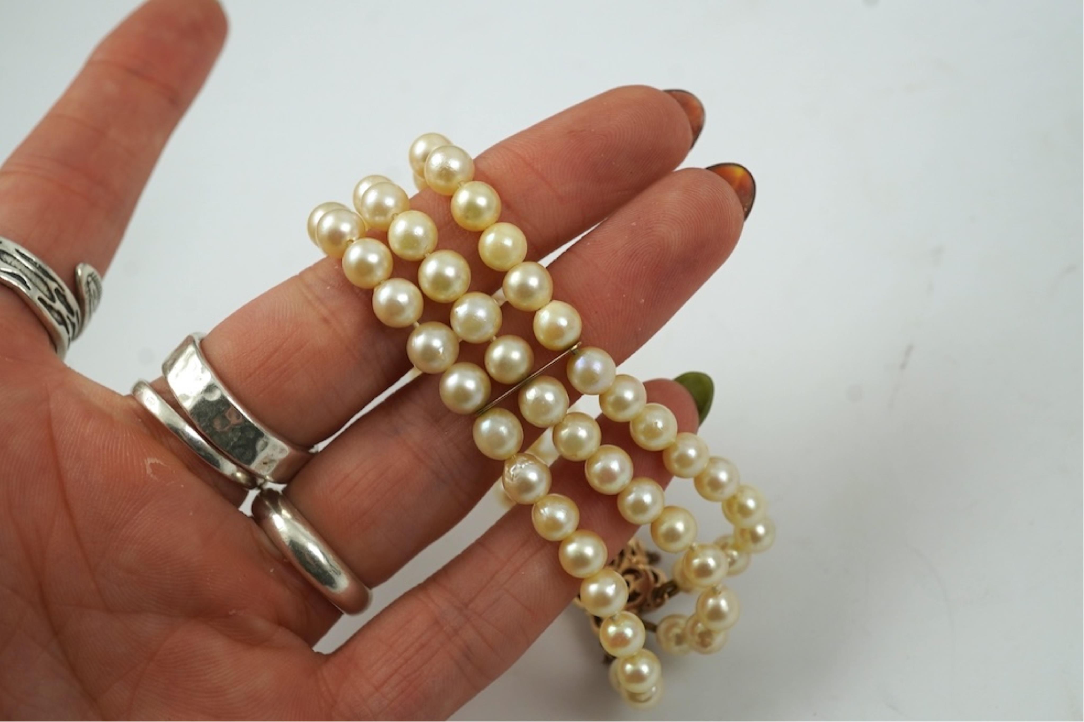 A triple strand cultured pearl bracelet, with a 9ct gold, garnet and cultured pearl cluster set clasp, 16cm.